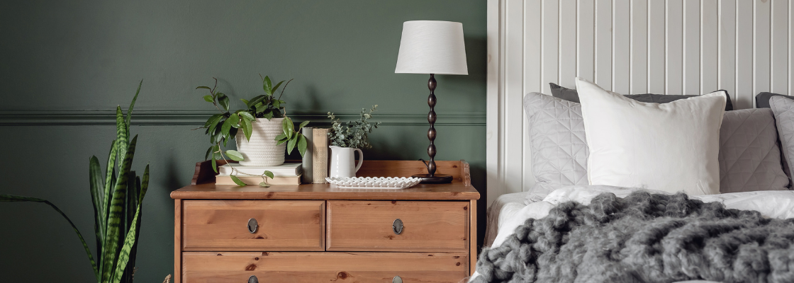 Schlafzimmer mit grüner Wand, Pflanzen, Kommode und Bett.